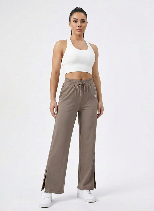 Woman wearing a white sports bra and brown drawstring pants on a white background